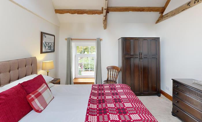 Another angle of the king bedroom at Ty Cerbyd showcasing exposed rafters, a skylight, and antique-style furniture, filled with natural light.